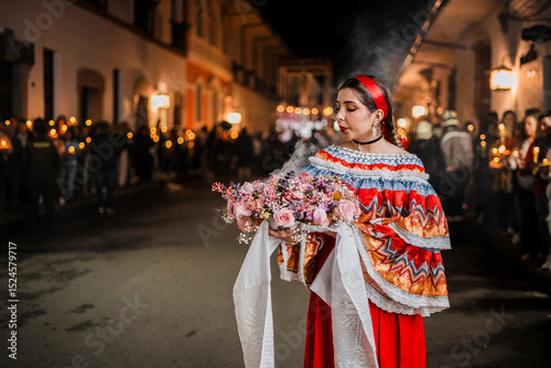 Mujer sahumadora vestida con traje típico tradicional participa en una procesión nocturna durante la Semana Santa en Popayán, Colombia. Sostiene un ramo de flores mientras esparce sahumerio 