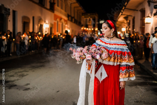 Mujer sahumadora vestida con traje típico tradicional participa en una procesión nocturna durante la Semana Santa en Popayán, Colombia. Sostiene un ramo de flores mientras esparce sahumerio 