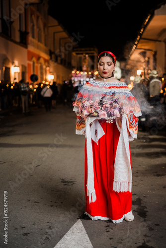 Mujer sahumadora vestida con traje típico tradicional participa en una procesión nocturna durante la Semana Santa en Popayán, Colombia. Sostiene un ramo de flores mientras esparce sahumerio 