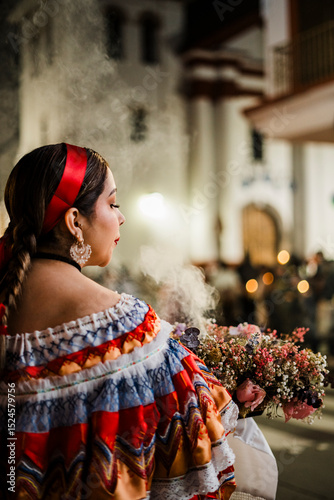 Mujer sahumadora vestida con traje típico tradicional participa en una procesión nocturna durante la Semana Santa en Popayán, Colombia. Sostiene un ramo de flores mientras esparce sahumerio 