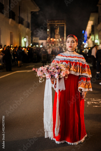 Mujer sahumadora vestida con traje típico tradicional participa en una procesión nocturna durante la Semana Santa en Popayán, Colombia. Sostiene un ramo de flores mientras esparce sahumerio 