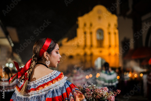 Mujer sahumadora vestida con traje típico tradicional participa en una procesión nocturna durante la Semana Santa en Popayán, Colombia. Sostiene un ramo de flores mientras esparce sahumerio 