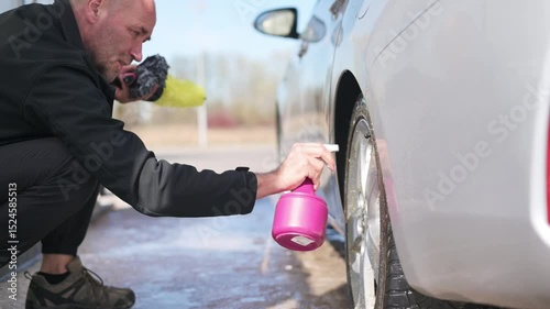 Spraying foam on wheel with bottle before scrubbing during car wash process