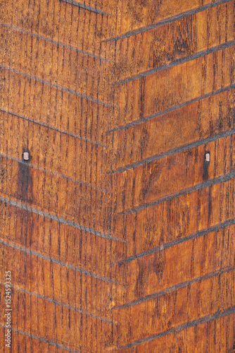 Close-up light brown wooden panel with inlaid herringbone pattern, visible nails, and varying shades of intricate wood grain. Image captures the rustic and textured appearance of weathered surface.