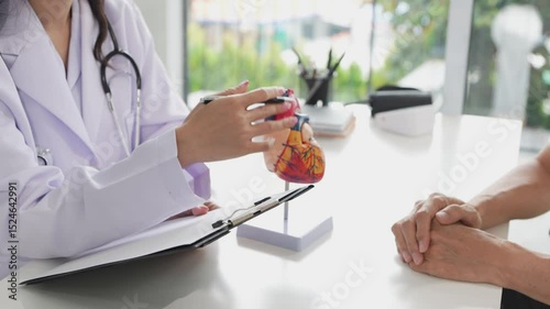 Elderly Asian male patient visits doctor for heart disease consultation. Doctor explains diagnosis at hospital to provide treatment to elderly man.