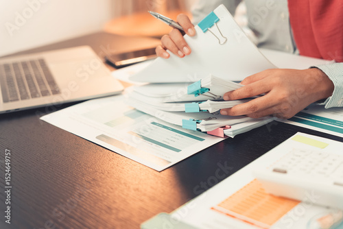 Professional woman checking charts and financial data with calculator and laptop and analyzing and reviewing. Close-up of young woman working with paper documents on desk.