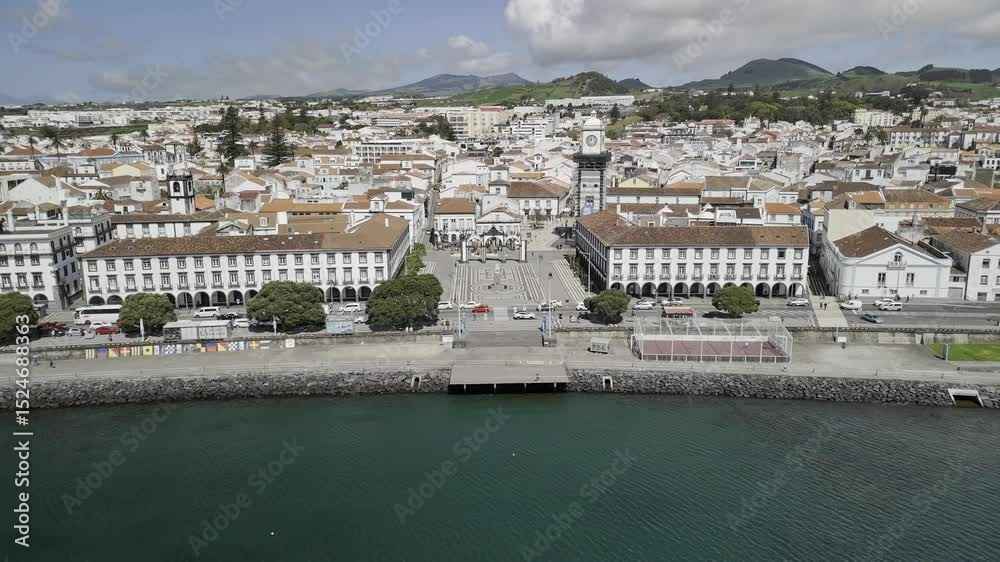 Drone flies north from boat marina toward the Portas da Cidade by the Igreja Matriz de Sao Sebastião on sunny day in Ponta Delgada, Sao Miguel, Azores, Portugal