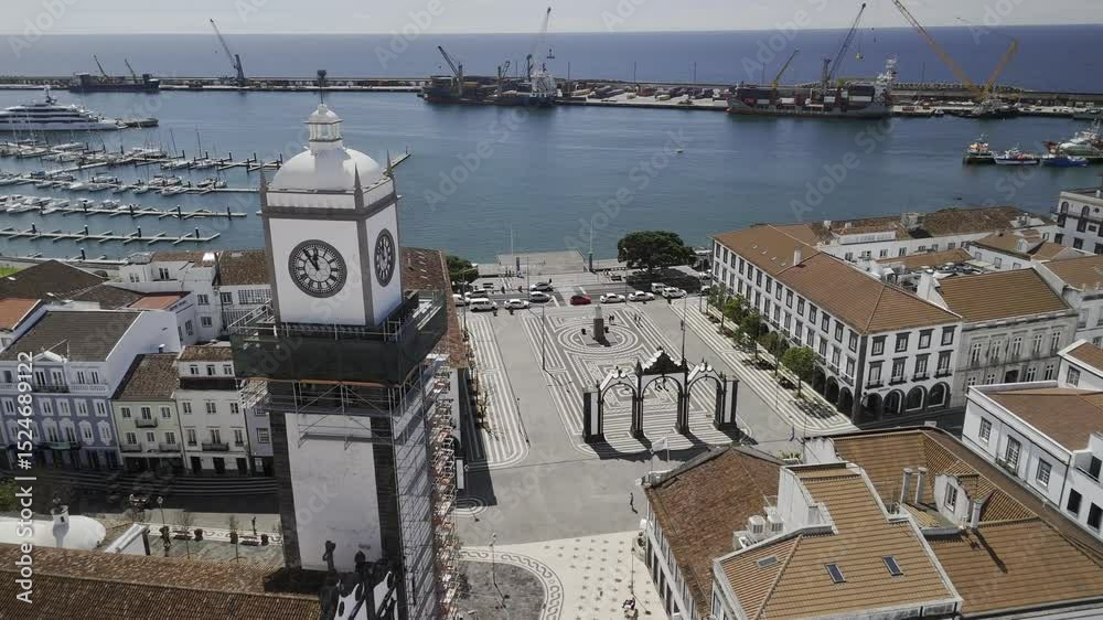 Drone flies south past Igreja Matriz de Sao Sebastião and the Portas da Cidade in historic city center on sunny day in Ponta Delgada, Sao Miguel, Azores, Portugal