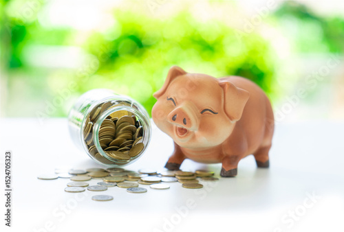 A piggy bank and a coin jar are placed together, with a pile of coins in front of them.
