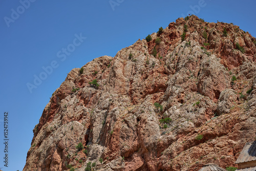 Scenic view of a rugged rocky cliff under a bright blue sky in a dry mountainous region. Natural textures, arid landscape, and distant hills create a stunning outdoor wilderness scene.