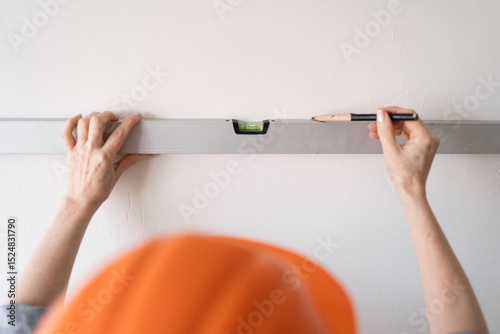 builder in an orange helmet making marks on a wall using a spirit level