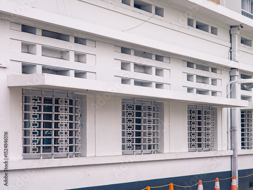Exterior of a white building featuring geometric ventilation blocks and barred windows with a symmetrical grid pattern, captured in soft daylight.