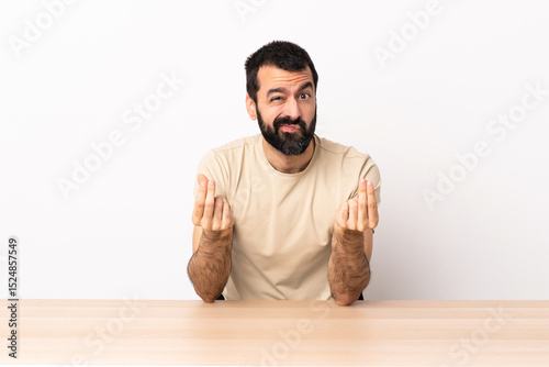 Caucasian man with beard in a table making money gesture but is ruined.