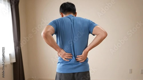 back view of an adult man holding and massaging his back and feeling pain