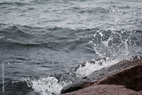 Fototapeta Naklejka Na Ścianę i Meble -  Close-up of splash of a small wave crashing on rocks on a cloudy day.