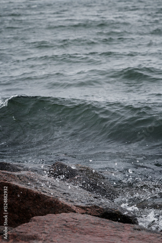Fototapeta Naklejka Na Ścianę i Meble -  Close-up of splash of a small wave crashing on rocks on a cloudy day.