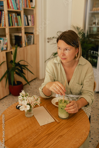 Middle-aged woman scrolls her social media feed on mobile phone in a cozy cafe. Small business. Using phone for business, online shopping, transfer money, financial, internet banking