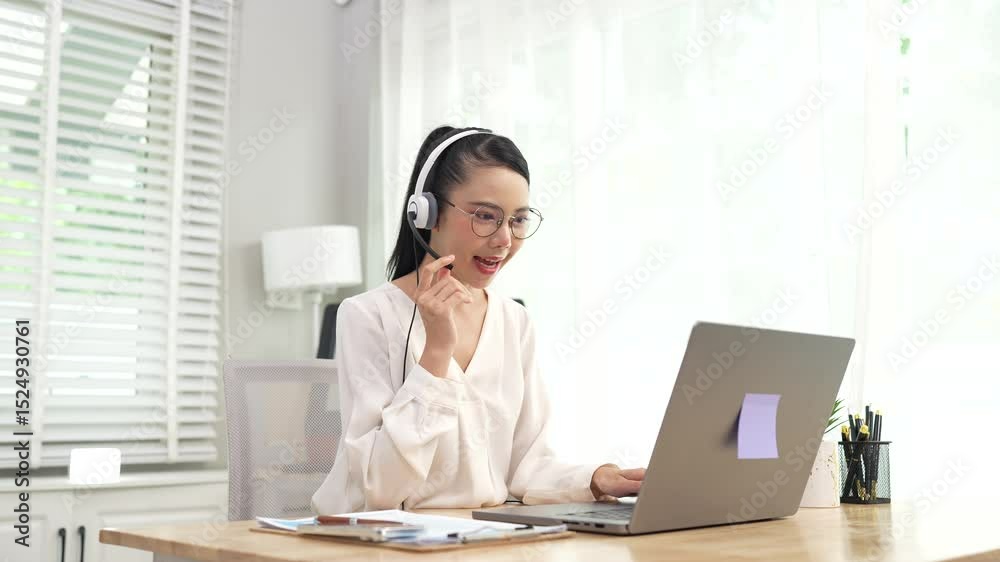 Smiling Asian female call center agent wearing a headset, speaking with a client at her office desk, providing professional customer support. Smiling Asian female call center agent wearing a headset, speaking with a client at her office desk, providing professional customer support.