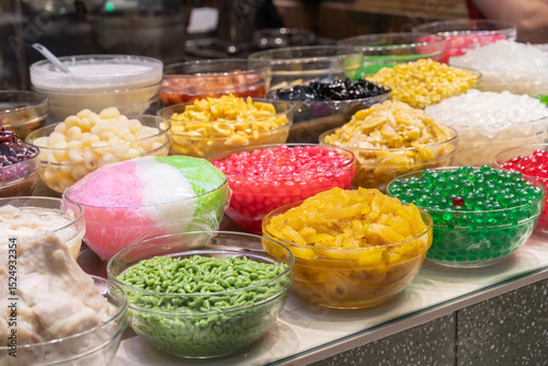 Colorful variety of toppings and ingredients commonly used in desserts, particularly in Southeast Asian and East Asian cuisine. These are often found at dessert stalls or shops.