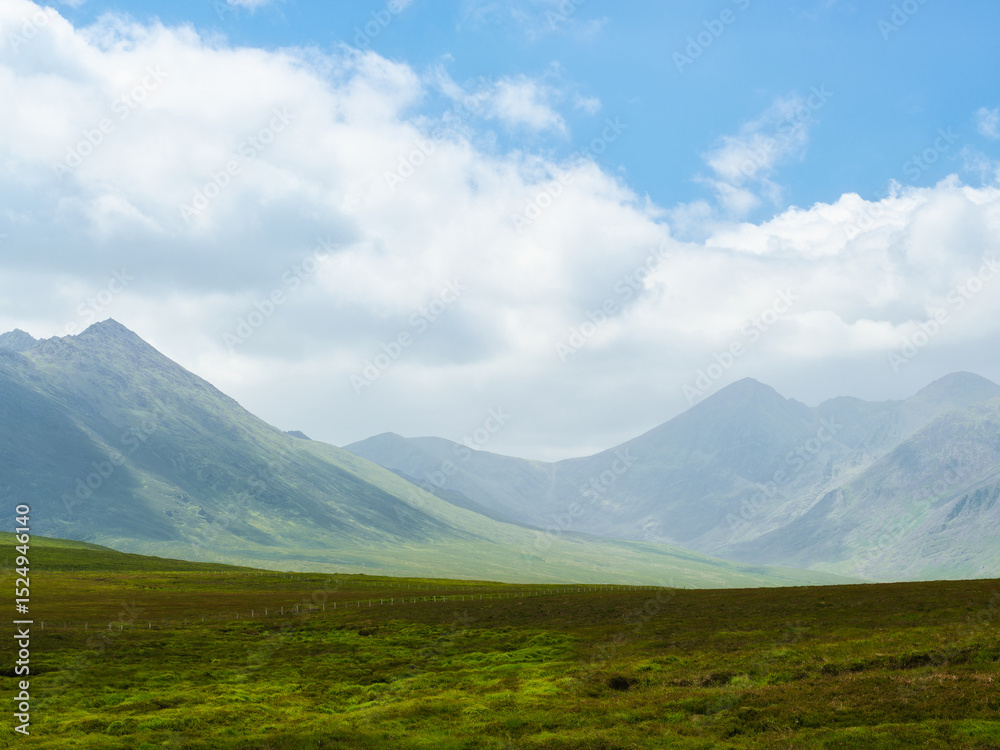 Fototapeta premium Serene vista of vibrant green pastures gently sloping towards imposing, dark mountain peaks. Nature's majestic beauty.