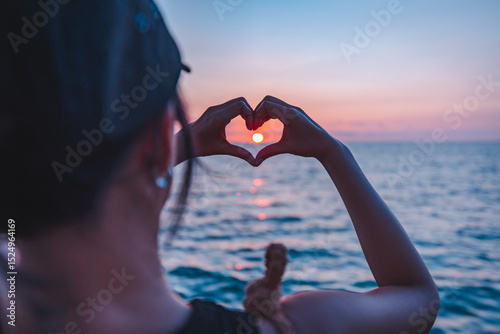 Happy asian traveler woman relax and making hand in heart love sign shape on sea beach at sunset in Koh Kood Trat Thailand Travel summer holiday vacation concept