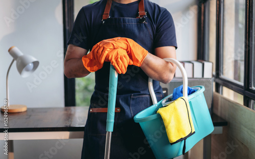 Housekeeping and cleaning concept, Happy young man in orange rubber gloves wiping dust using mop while cleaning on floor at home
