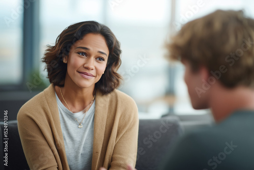 An empathetic therapist of South Asian descent sits in a calm, sunlit office, actively listening to a young Caucasian male client who is expressing his feelings.