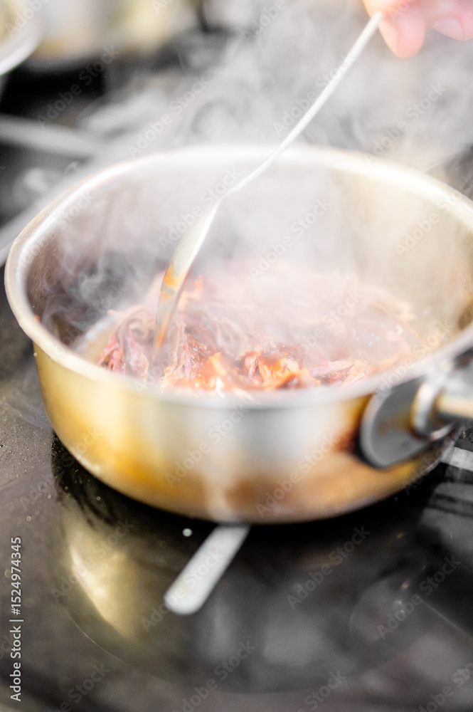 custom made wallpaper toronto digitalA steaming stainless steel pan with meat cooking on a stovetop. A hand stirs the ingredients with a spoon, showcasing active food preparation in a kitchen setting