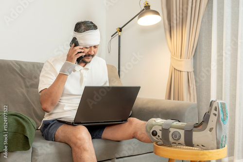 Smiling man with leg in cast works remotely at home using a laptop.