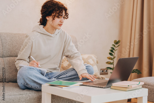 Teen student girl studying at home using laptop and taking notes