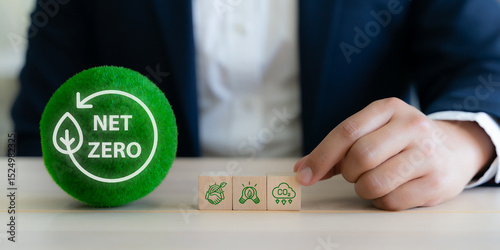 Net Zero, sustainable business strategy concept. Hand arranging wooden blocks with sustainability icons with green sphere labeled "Net Zero". Corporate commitment to environmental responsibility.