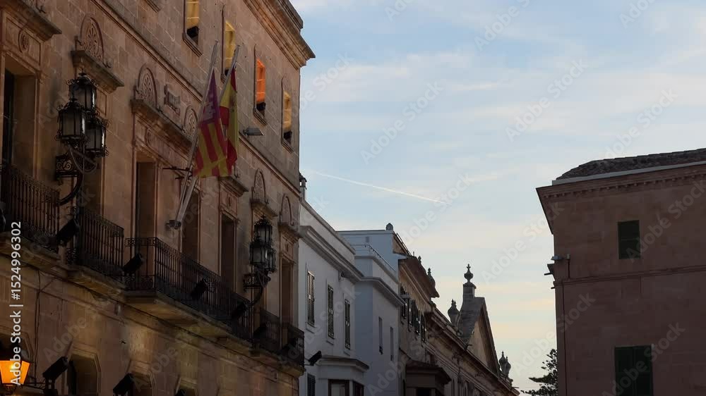 Stunning shot of Parroquia de Nuestra Señora del Roser in Ciutadella, Menorca with the warm evening light highlighting its historic facade and beautiful balconies, accompanied by the regional flags. Stunning shot of Parroquia de Nuestra Señora del Roser in Ciutadella, Menorca with the warm evening light highlighting its historic facade and beautiful balconies, accompanied by the regional flags.