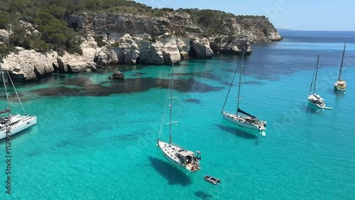Wallpaper Mural Sailboats anchored in the crystal-clear turquoise waters of Cala Macarella, Menorca, surrounded by limestone cliffs and lush Mediterranean vegetation on a sunny summer day. Torontodigital.ca