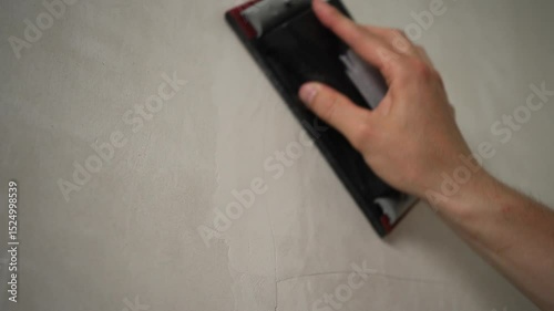 Professional worker sands a gray wall with a hand sander to level the surface and prepare it for painting, ensuring a smooth and even finish