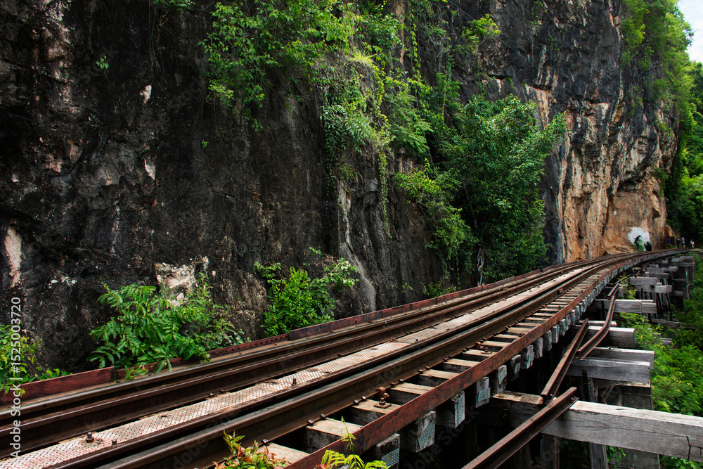 Obraz premium Train railway track between hellfire pass mountain and Si Sawat or Khwae Kwai river with forest jungle wildness in Sai Yok National Park for travel visit at Tham krasae cave in Kanchanaburi, Thailand