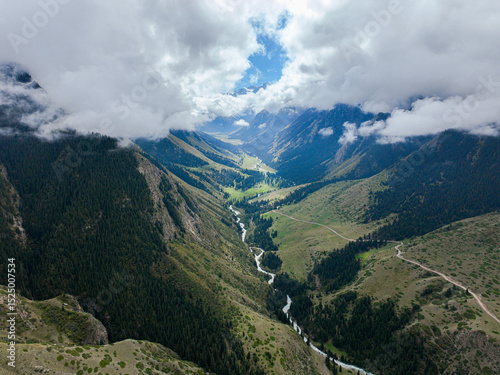 An aerial view capturing a winding river carving its way through a verdant mountain valley, flanked by lush green slopes under a cloudy sky