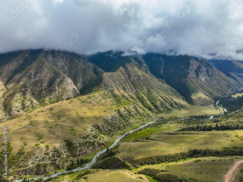 An aerial view showcases a lush green mountain landscape with a river meandering through the valley, under a cloudy sky