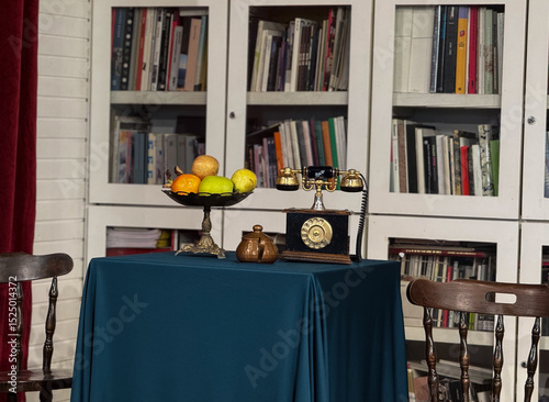 Vintage rotary telephone and fruit bowl on elegant table in front of bookshelf. Classic interior detail in cozy retro-inspired reading room.