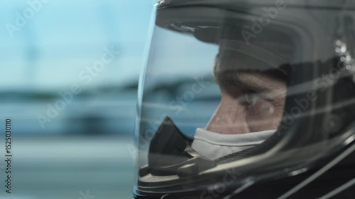 Close-up of focused race car driver wearing helmet and balaclava, staring ahead while driving at high speed on sunny day at professional racing circuit. Action motorsport video.