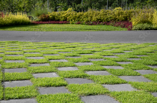 Checkered pattern of green grass and cement tiled floor with walkway and decorated garden photo