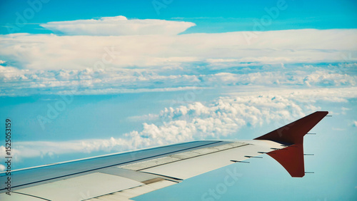 Aircraft wing soaring through pristine white clouds against vibrant blue skyline