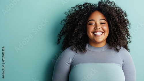 Young woman with curly hair smiling against a teal background