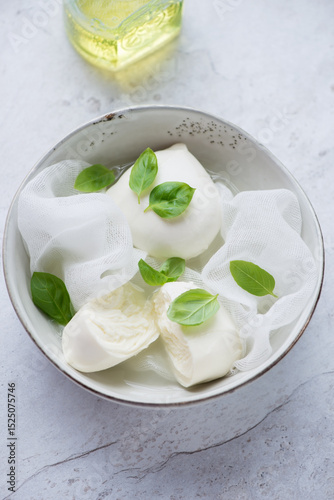 Bowl with freshly made buffalo mozzarella and green basil on a white stone background, elevated view, vertical shot