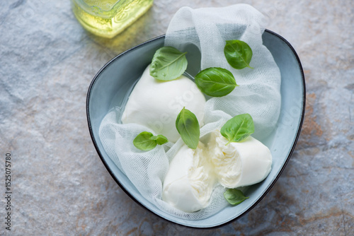 Buffalo mozzarella in brine with green basil leaves, horizontal shot on a beige and blue stone background, elevated view