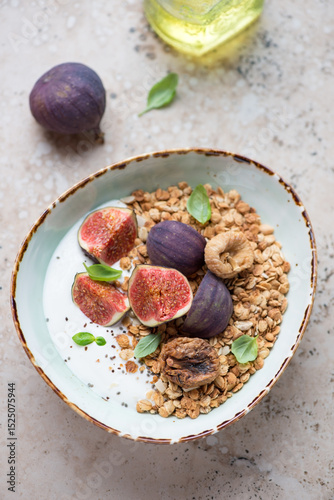 Bowl with granola, fresh and dried figs and greek yogurt, vertical shot on a beige granite background, elevated view