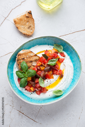 Turquoise bowl with ricotta dip, chopped tomatoes and ciabatta, vertical shot on a white stone background, elevated view