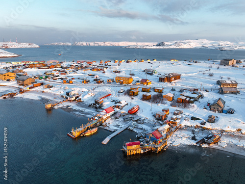 Aerial view of Teriberka village, with snow-covered houses and boats along the shore of the Barents Sea, Russia