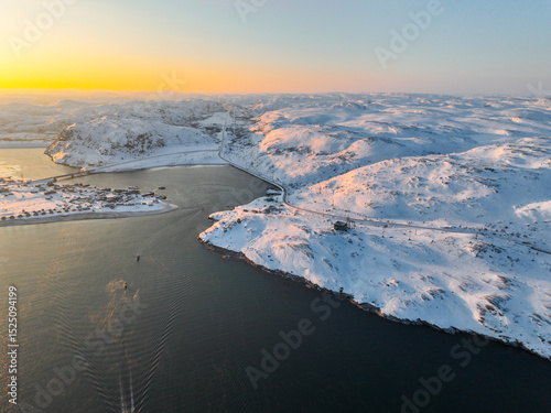 Expansive aerial view of Teriberka's snow-covered landscape, featuring a river and a winding road in winter, Russia