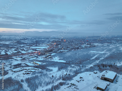 Wide aerial view of the snow-blanketed city of Murmansk, surrounded by winter forests and distant hills, Russia