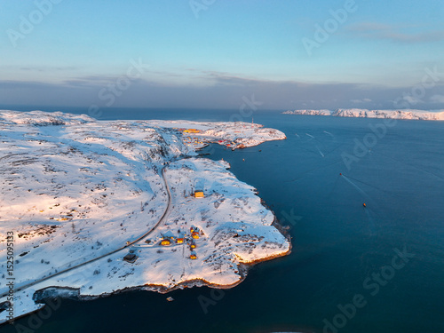 Panoramic aerial view of a snowy coastal village nestled among hills leading to the open sea in Teriberka, Russia